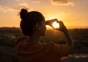 A silhouette of a young woman forming a heart shape at sunset in Kelâat M'Gouna, Morocco.