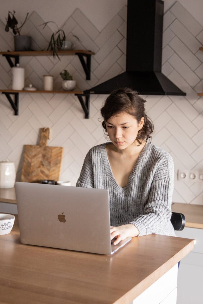 Young woman using laptop at kitchen counter with milk and a bowl.