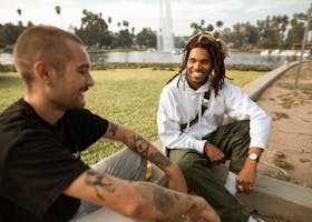 Two men sitting and smiling together by the lake, enjoying a sunny day outdoors.