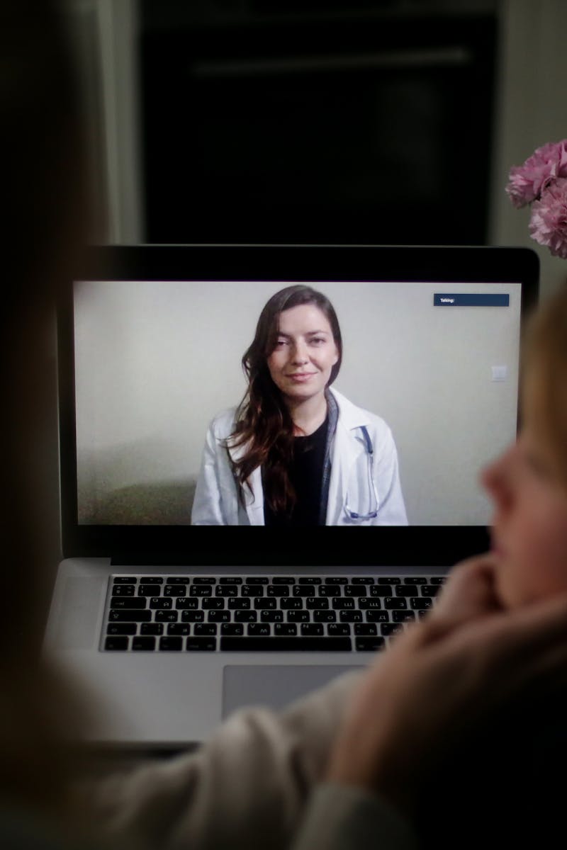 A doctor appears on a laptop screen during an online medical consultation at home.
