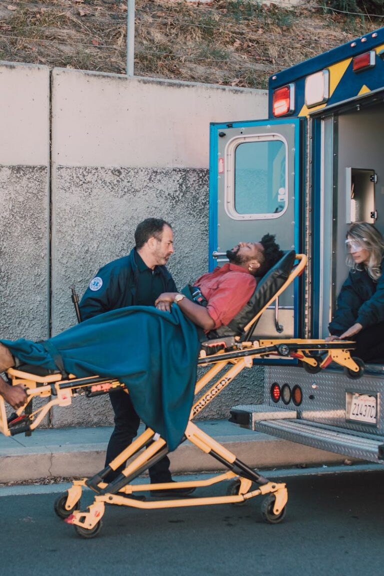 First responders assist an injured man onto a stretcher and into an ambulance during a daytime emergency call.