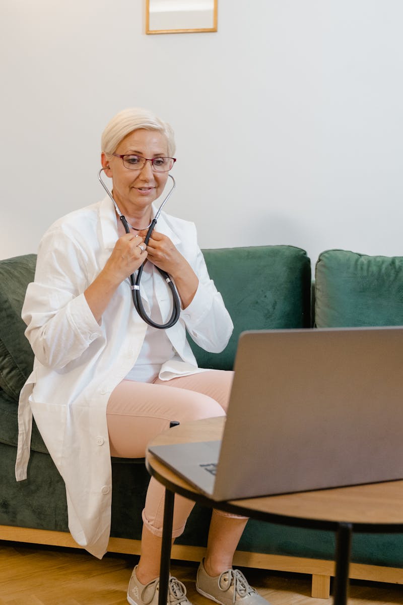 Female doctor in a white coat conducting an online consultation from home using a laptop.